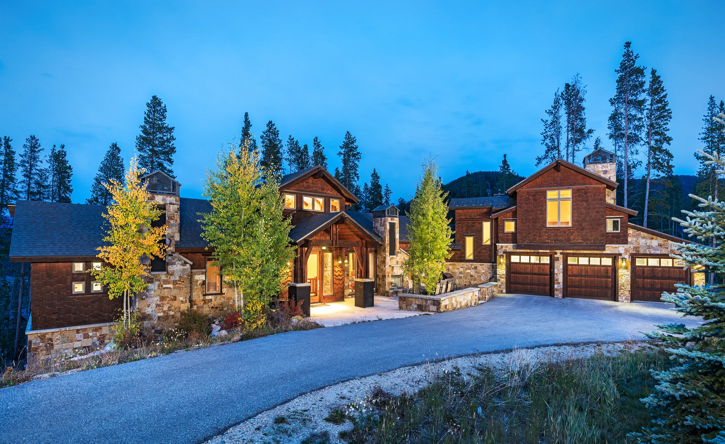 Mountain home with stone and timber details surrounded by autumn trees at dusk