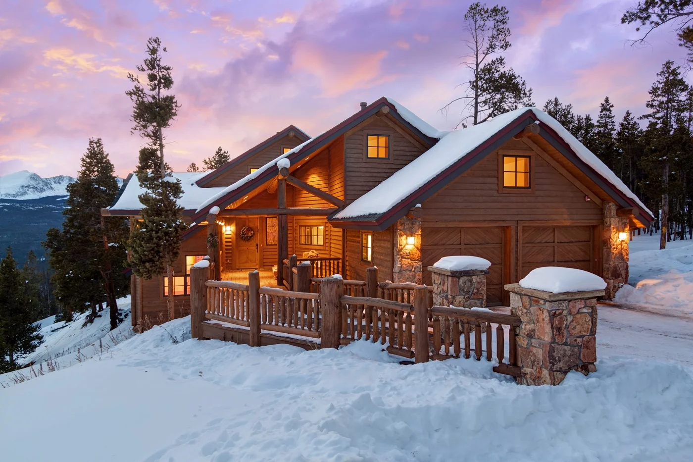 Snow-covered mountain home with a timber deck at dusk