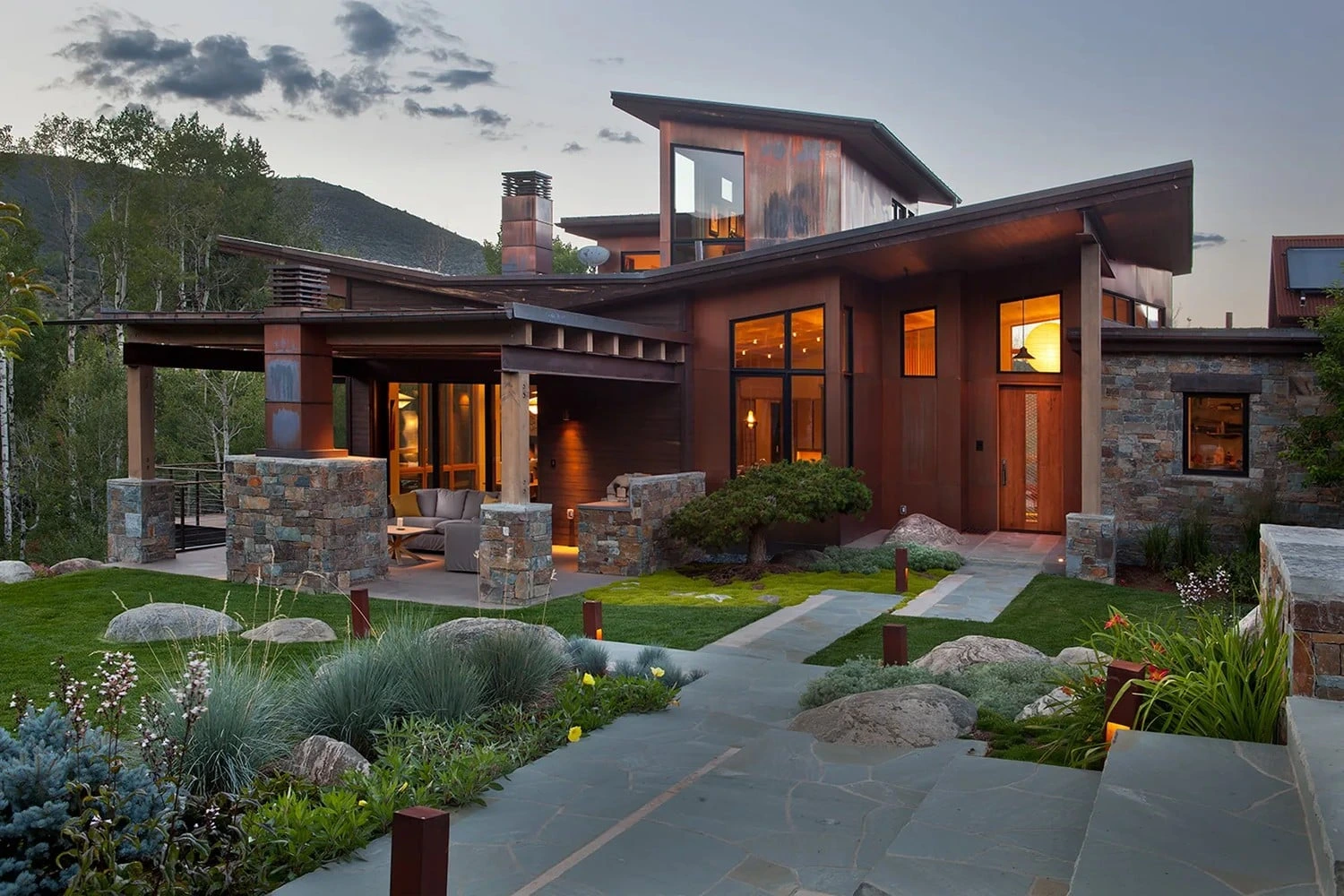 Vail Valley home with warm-lit windows, stone columns, and landscaped gardens