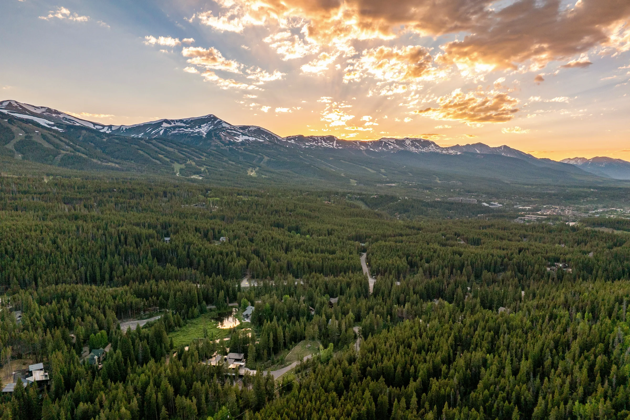 Aerial view of forested mountain terrain beneath a glowing sunset
