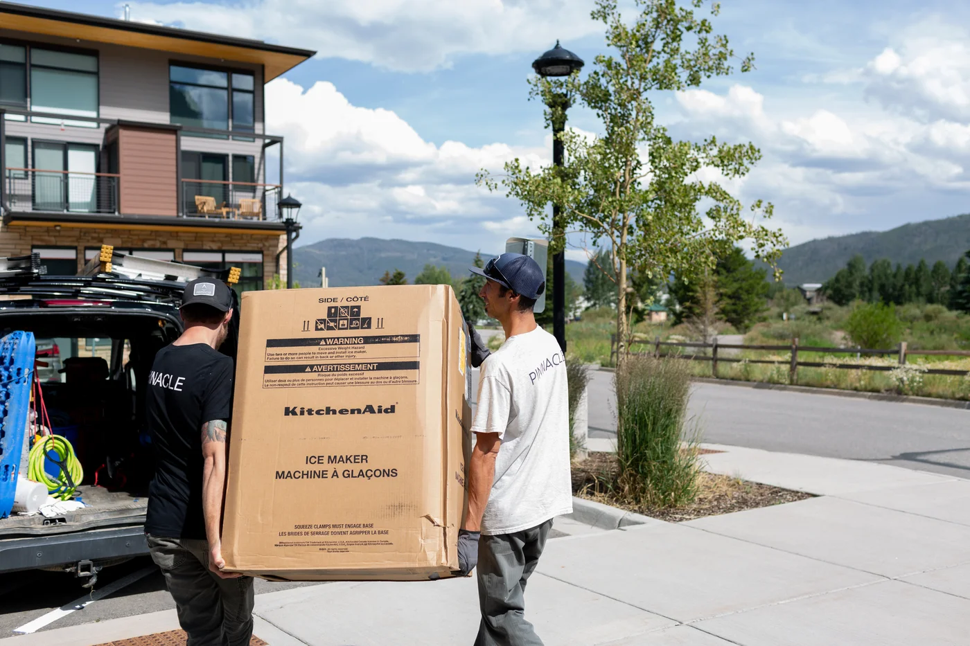 Pinnacle Lodging team members carrying a boxed appliance beside their work vehicle